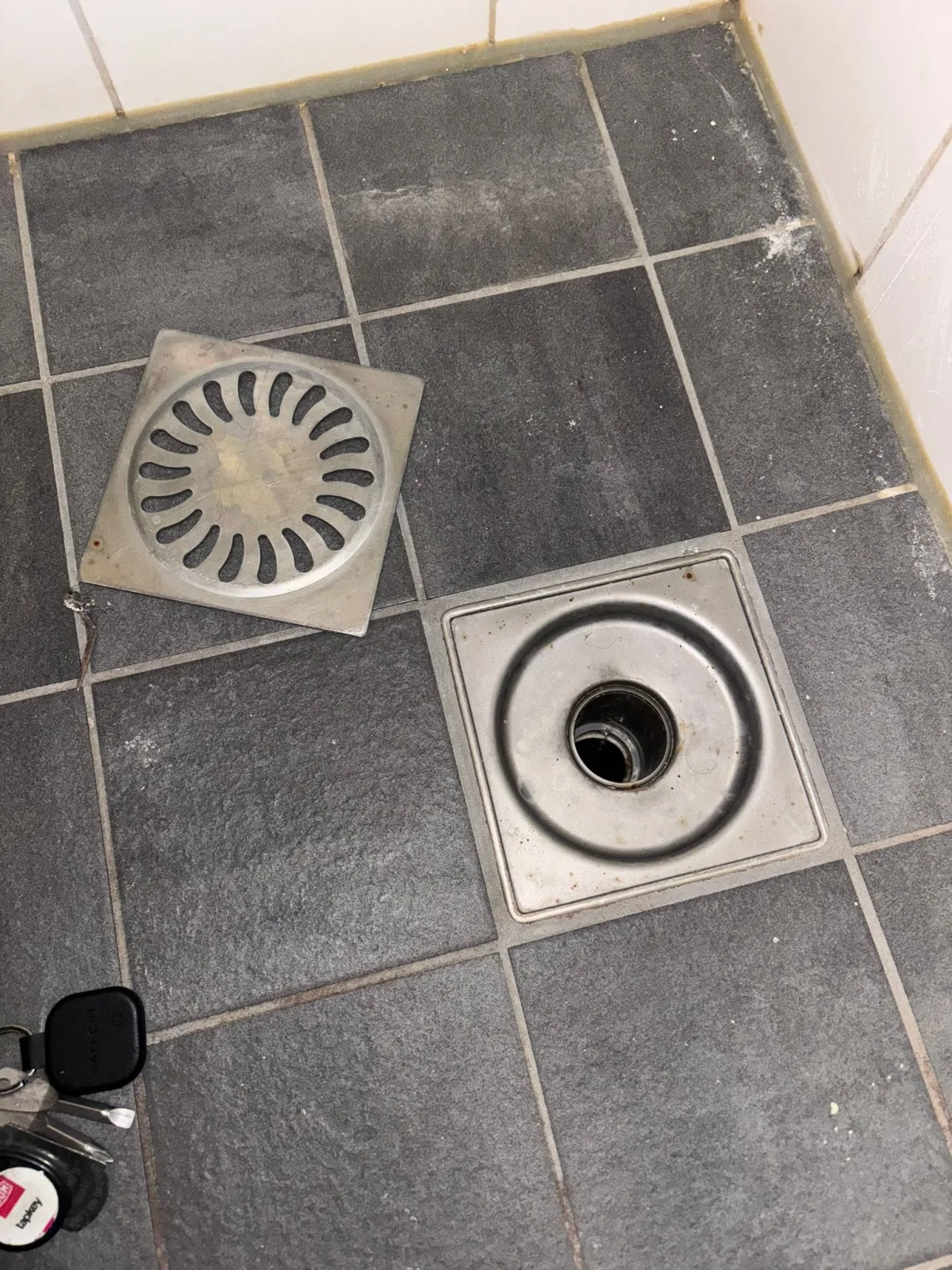 Twee vloerputten in betegelde ruimte, één open met deksel ernaast, duidend op inspectie.